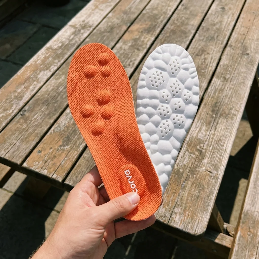 Angela P. holding up a pair of CloudStep insoles at a wooden picnic table outdoors — coral top and sculpted white underside both visible