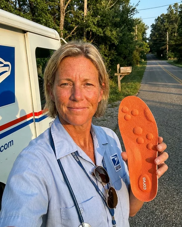 Michelle S., rural mail carrier, holding up a CloudStep insole next to her USPS delivery truck on a country road